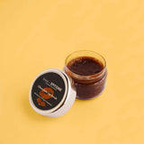 Chocolate Lip Scrub in an open clear jar, with dark brown scrub and a white lid featuring a black label.